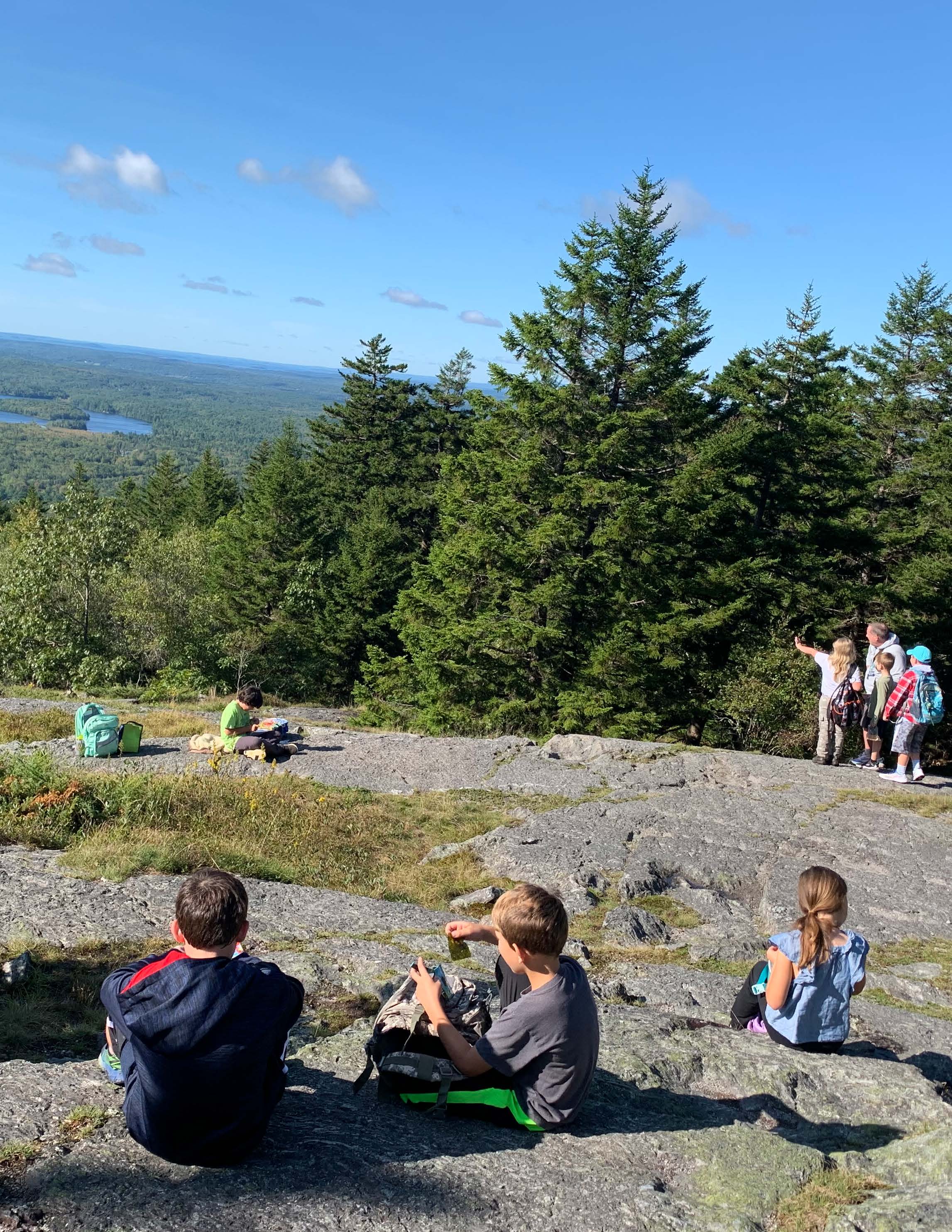 Students and teachers on a rocky hilltop looking out in the distance