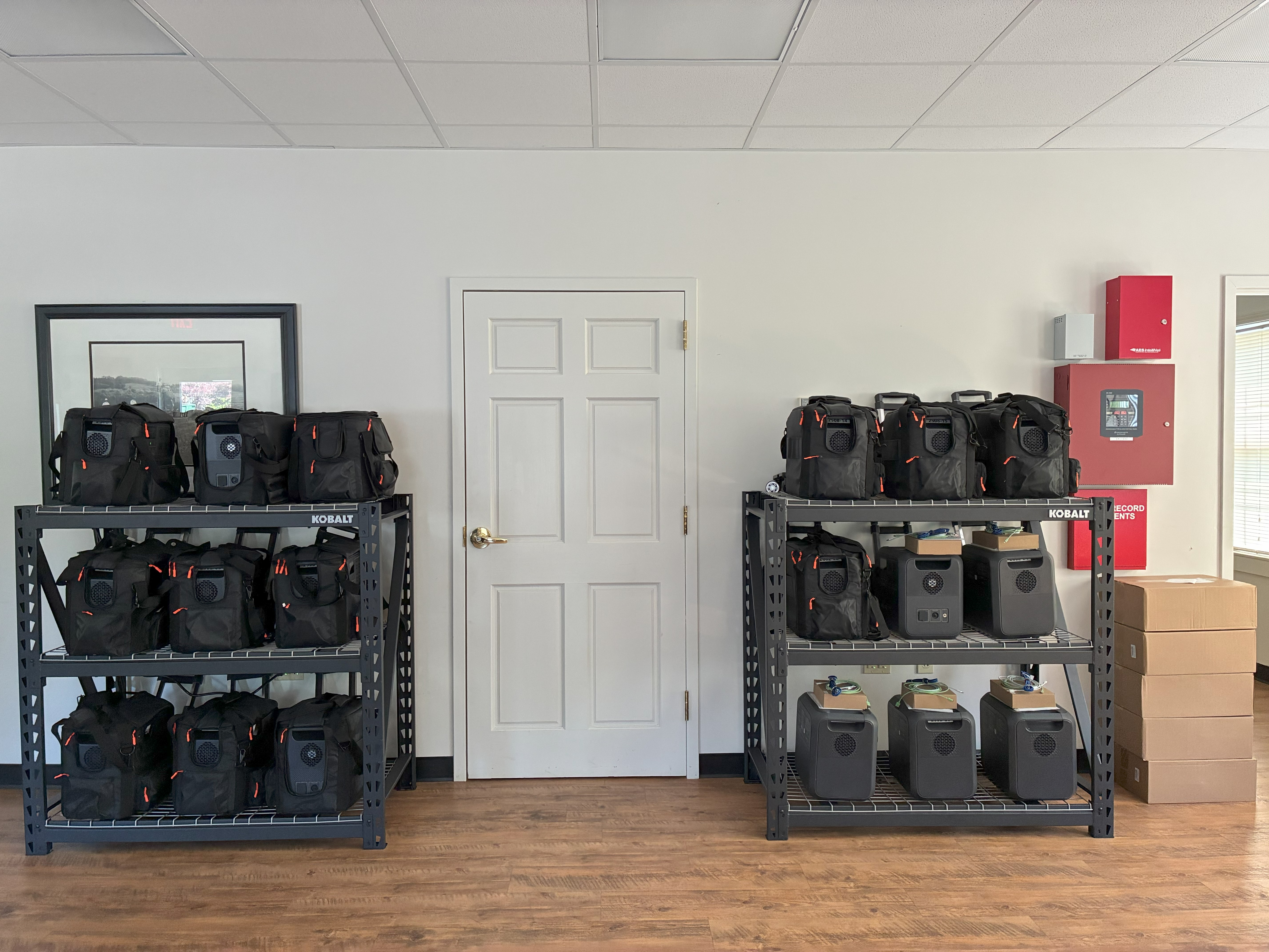 Two shelving units with black bags in a white walled room.
