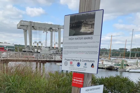 A high water mark sign with boats in the background.